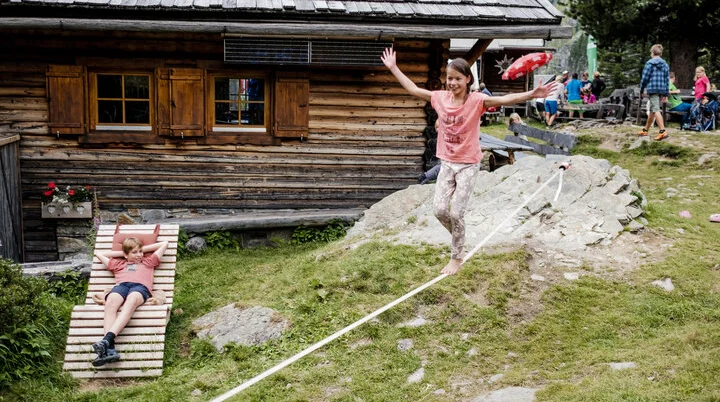 Mit Kindern in den Bergen | © DAV/Hans Herbig Zwei Kinder balancieren auf einem Seil, das vor einer Berghütte gespannt ist | © DAV/Hans Herbig